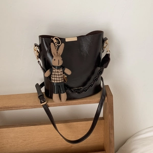 Detail of glossy black bucket bag with gold hardware and brown knit rabbit charm