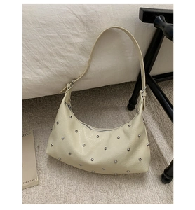 Close-up of beige hobo bag with silver studs on soft textured carpet background