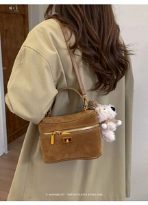 Détail du sac boîte en daim marron avec boucle dorée et breloque chien sur un trench-coat
