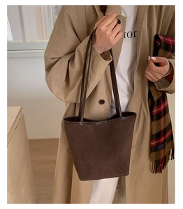 Close-up of brown suede bucket bag texture styled with a trench coat and scarf