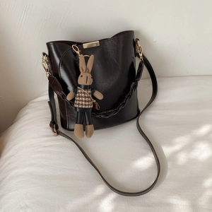Detail of a vintage dark leather bucket bag featuring a knit rabbit charm and gold buckle