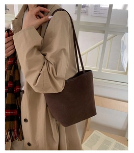 Close-up of a brown suede bucket bag worn over the shoulder with a stylish autumn outfit