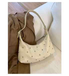 Close-up detail of cream crescent shoulder bag featuring silver rivets on matte leather