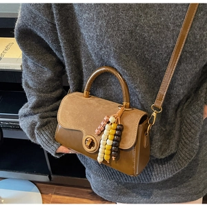 Detail of a brown leather crossbody bag with suede flap, metal lock, and wooden bead charm