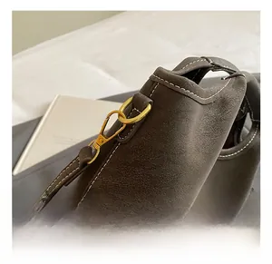 Close-up of golden metal hook on dark brown suede bucket bag with white contrast stitching