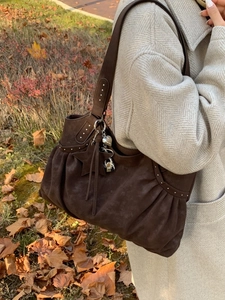 Brown suede tote bag with star charms and silver rivets shown on outdoor model