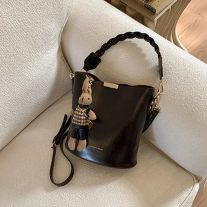 Detail of dark brown bucket bag with woven handle and knitted rabbit charm on a sofa