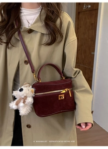 Détail du sac boîte en daim bordeaux foncé avec finitions dorées et breloque ours