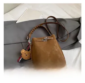 Detailed view of brown suede bucket bag with woven handle and plush bear charm