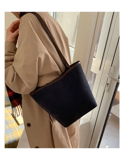 Detailed side view of navy suede bucket bag with brown leather trim on beige trench coat