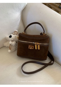 Détail du sac boston en daim marron avec fermoir doré posé sur un canapé beige