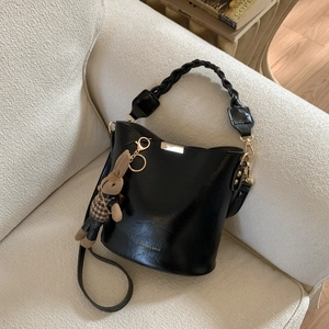 Detail of black glossy leather bucket bag with woven handle and cute rabbit pendant