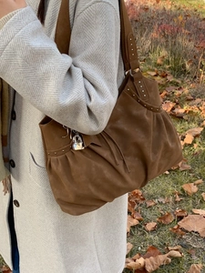 Brown faux suede tote bag with rivets and lock charm shown with autumn coat