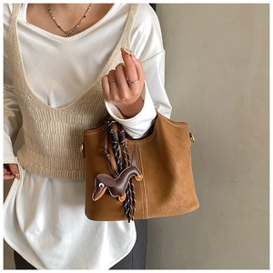 Detail of a brown frosted bucket bag with white stitching and a dachshund charm
