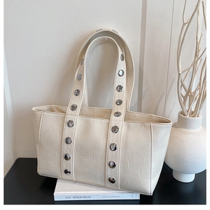 Detail of creamy white tote bag featuring large silver studs on textured leather