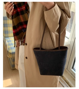 Detail of dark blue bucket bag with brown leather trim styled with an autumn trench coat