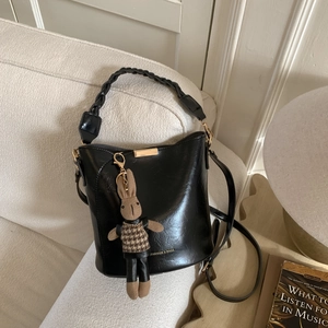 Close-up of black bucket bag with woven handle and cute rabbit charm on a sofa