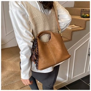 Close-up of brown textured leather bucket bag with white contrast stitching and silk scarf