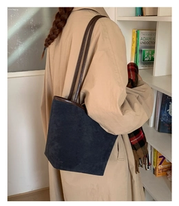 Detailed view of a navy suede tote bag with brown leather straps in a lifestyle setting