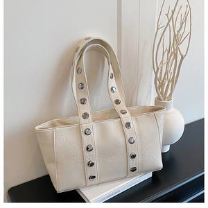 Detail of off-white tote bag featuring silver rivet studs and textured leather finish