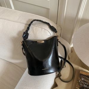 Detail of black leather bucket bag with braided handle and gold metal hardware accents