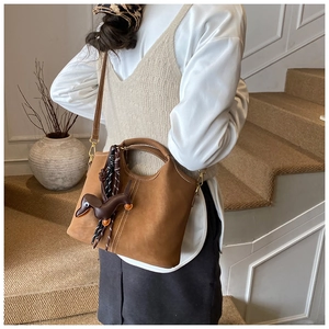 Detail of a brown suede bucket bag featuring a cute dachshund leather charm attachment