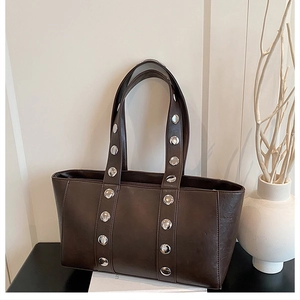 Close-up of deep brown leather tote bag featuring double rows of large silver rivets