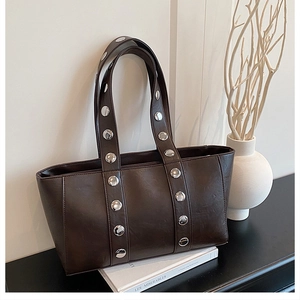 Detail of dark brown leather tote bag with large silver metal rivets in punk style