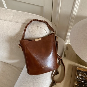 Detail of a brown leather bucket bag with a woven handle on a cozy sofa setting