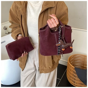Detail of burgundy matte leather bucket bag set with white stitching and dog charm