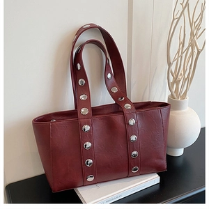 Detail of burgundy leather tote bag with silver metal studs on a minimalist background