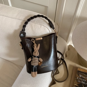 Detail of a brown leather bucket bag with braided handle and cute rabbit charm on a sofa