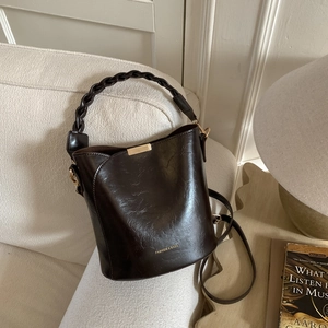 Detailed macro of dark brown leather bucket bag featuring a woven handle and gold hardware