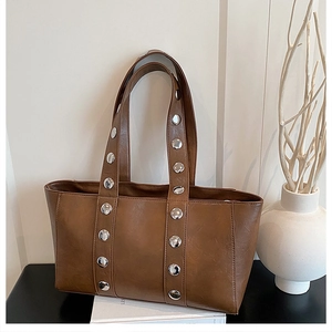 Detail of a brown tote bag featuring silver rivet decorations in a stylish lifestyle setting