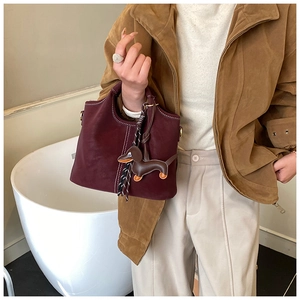Detail showing burgundy matte leather handbag with white stitching and dog charm
