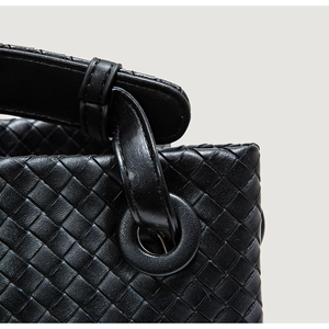 Detailed close-up of premium black woven leather texture and reinforced handle attachment