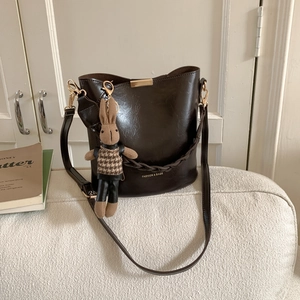 Detail of dark brown glossy bucket bag featuring gold lettering and cute bunny charm