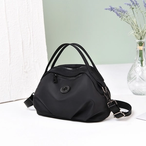 Detail of a black nylon crossbody bag with dual handles and adjustable strap on a white table