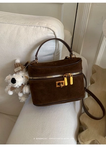 Détail du sac boîte en daim marron foncé avec ferrures dorées et breloque chiot peluche