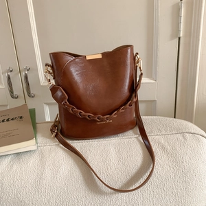 Macro detail of brown leather bucket bag with gold hardware and woven handle on sofa