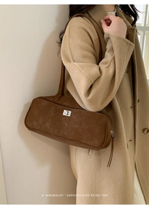 Detalle del bolso baguette de ante marrón con cierre de giro plateado sobre modelo