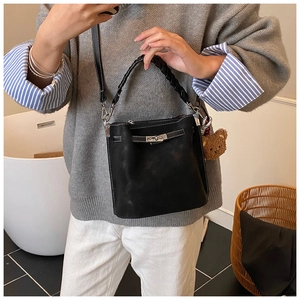 Detail of black leather bucket bag with woven handle, metal lock, and plush bear charm
