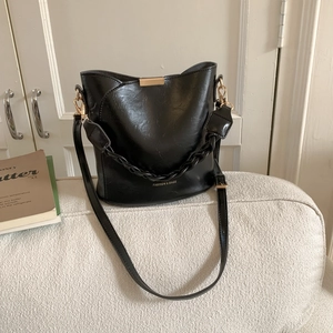 Detail view of black minimalist bucket bag with gold accents and woven chain handle