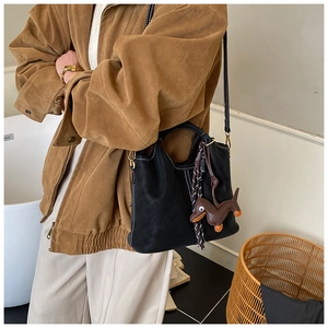 Detail of black matte bucket bag with white stitching, dog charm and tassel detail