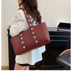 Detail of burgundy leather tote bag with silver metal studs in a modern office setting