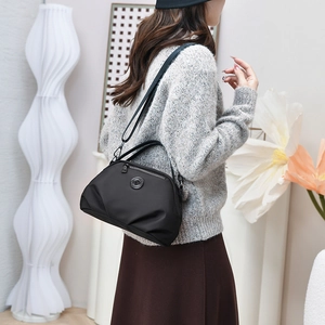 Detail of black nylon shoulder bag showing matte texture and circular logo on front pocket