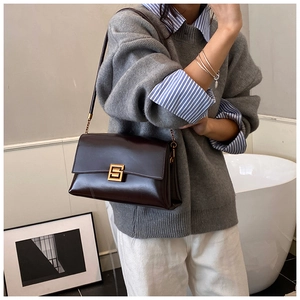 Detailed view of deep brown glossy leather shoulder bag with gold square metal buckle