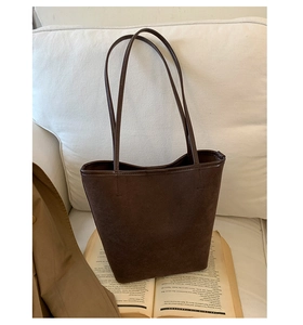 Detailed close-up of dark brown suede bucket bag on sofa with aesthetic book and coat