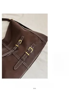 Détail d'un sac bandoulière en cuir marron foncé avec sangles à boucles et coutures contrastées