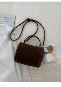 Vue de dessus sac boîte en daim marron avec breloque ours sur tissu blanc texturé